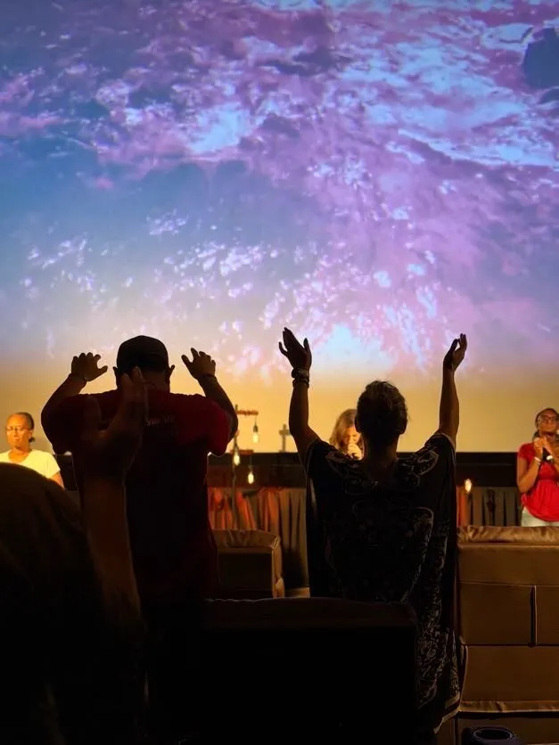 Silhouettes of worshippers with hands raised against a sunset-colored screen