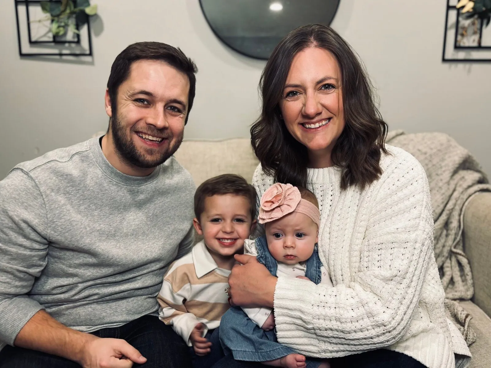 Pastors Luke and Laura Simpson smiling on the couch with their two children